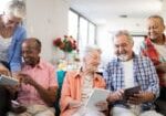 Happy senior people using tablet computers while sitting on sofa at nursing home